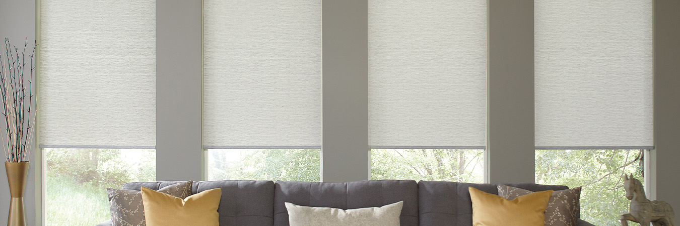 Light gray window shades on four living room windows behind a gray sofa