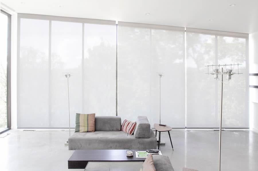 Motorized window shades make controlling natural light effortless in your Hartford great room. White motorized shades on a wall of tall great room windows
