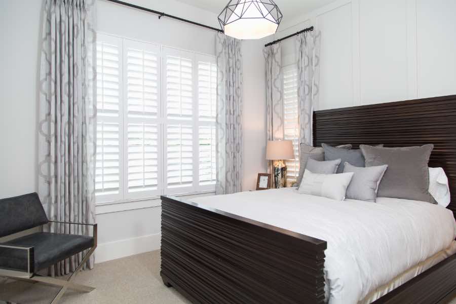 New window treatments are the perfect finishing touch to any room makeover! White Polywood shutters on windows in a stylish bedroom