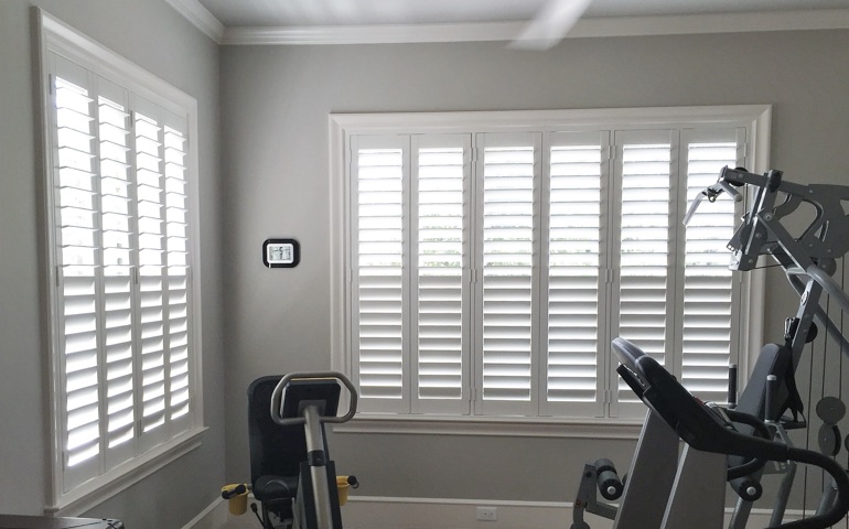 Draft-blocking window treatments are vital in spaces with windows on multiple walls. Hartford fitness room with shuttered windows.