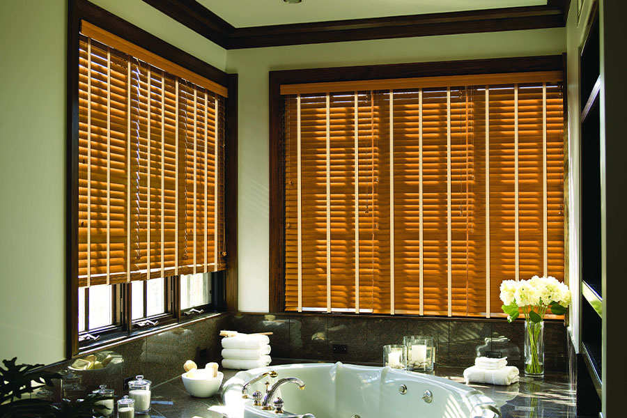 Premium wood shutters last longer than cheap blinds, even in humid environments! Brown wood shutters on large windows in a green bathroom